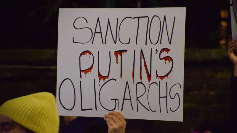 Ein Londoner Demonstrant hält ein Plakat hoch mit der Aufschrift "Sanction Putin's Oligarchs"