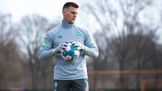 Werders Ersatztorwart Michael Zetterer steht am Rande des Trainings und hält einen Ball in den Händen.