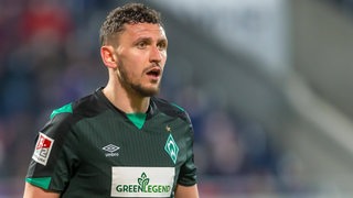 Werder-Verteidiger Milos Veljkovic steht mit verwundertem Blick und offenem Mund auf dem Spielfeld.