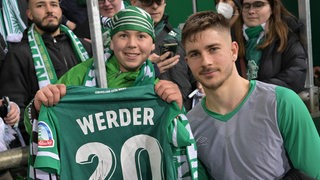 Romano Schmid posiert nach dem Spiel mit einem jungen Werder-Fan, dem er sein Trikot geschenkt hat.