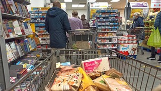 Ein mit Lebensmitteln gefüllter Einkaufswagen steht in einer Supermarkt-Schlange.
