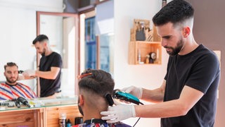 Ein Friseur trimmt einem Kunden die Haare.