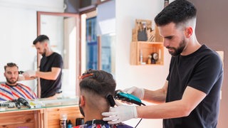Ein Friseur trimmt einem Kunden die Haare.