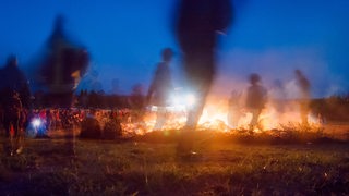 Menschen laufen in der Dämmerung um ein Osterfeuer