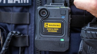 Eine Bodycam hängt an der Schutzweste einer Polizeiuniform.