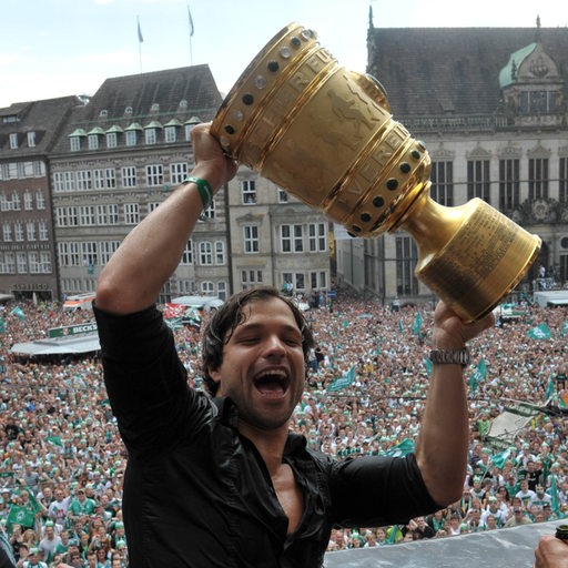 Diego reckt auf dem Bremer Rathaus-Balkon den DFB-Pokal jubelnd in die Höhe, hinter ihm tausende Werder-Fans auf dem Marktplatz.