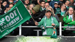 Blick auf die Tribüne mit enttäuschten Werder-Fans, ein älterer Herr hält traurig eine grün-weiße Fahne.