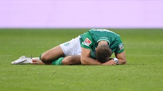 Werder-Stürmer Niclas Füllkrug liegt nach der Niederlage auf dem Rasen, den Kopf auf seine Hände gelegt.