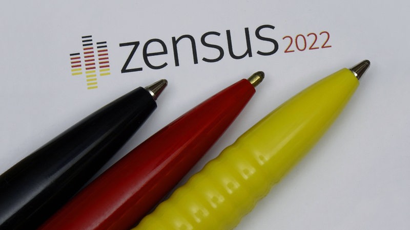 Auf einem Blatt Papier mit der Aufschrift "Zensus 2022" liegen drei Kugelschreiber in den Deutschland-Farben