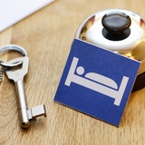 An einer Klingel lehnt ein Schild mit einem Bett darauf, daneben liegt ein Schlüssel