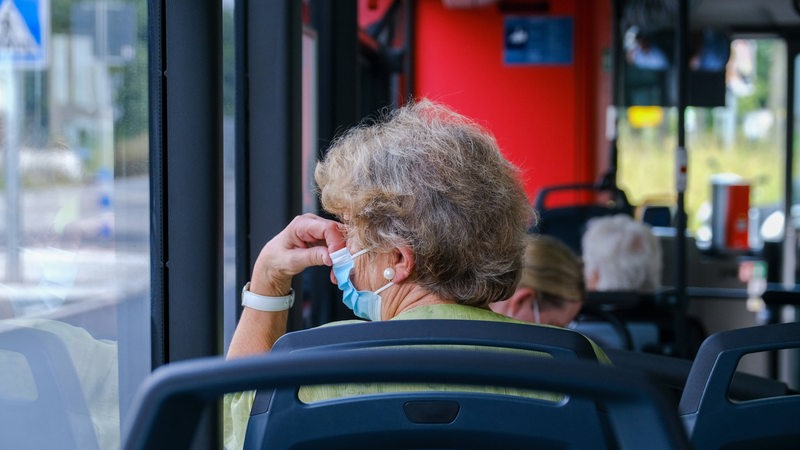A woman sits on a bus wearing a mask.