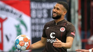 Daniel-Kofi Kyereh vom FC St. Pauli trägt im Spiel mit breitem Lächeln den Ball in der Hand.
