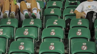 Grüne Sitze in einem Fußball-Stadion mit aufgeklebten Nichtraucher-Schildern.