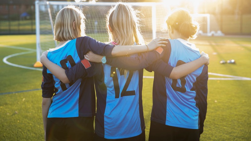 Drei junge Fußballerinnen stehen nebeneinander und legen sich die Arme über die Schultern.