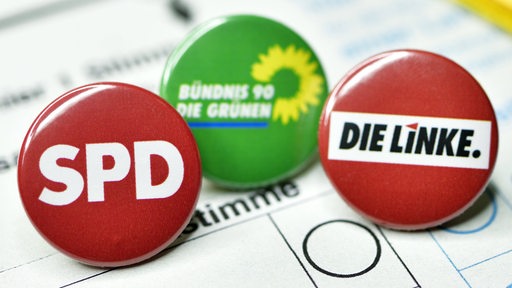 Drei Buttons mit dem Logos von SPD, Grüne und Linken liegen auf einem Wahlzettel.