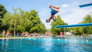 Ein Junge springt einen Salto von einem ein Meter-Brett.