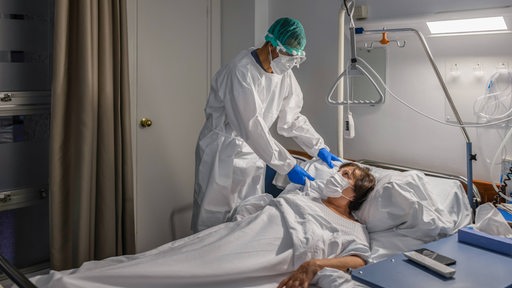 Ein Pfleger mit Mundnasenschutz behandelt eien Krankenhaus-Patientin