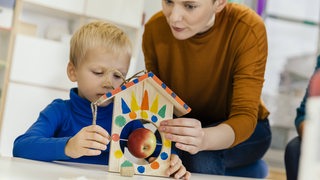 Ein kleiner Junge baut mit einer Kindergartenerzieherin eine Futterstelle für Vögel.