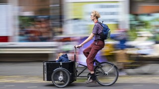 Eine Fahrradfahrerin ist mit einem Lastenrad und Kind unterwegs in Berlin.