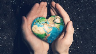 Zwei Hände wiegen eine Erde in Herzform. 