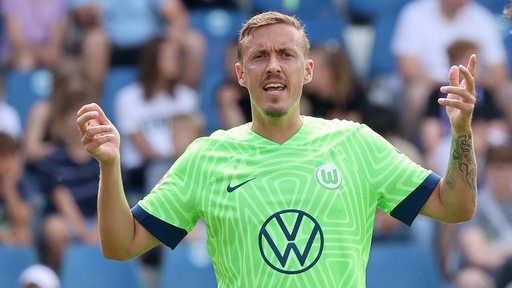 Wolfsburg-Spieler Max Kruse gestikuliert auf dem Spielfeld und reckt beide Arme hoch.