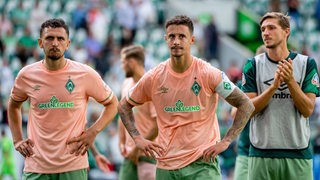 Werder-Spieler Milos Veljkovic und Marco Friedl stützen nach dem Unentschieden in Wolfsburg nachdenklich die Hände in die Hüften.
