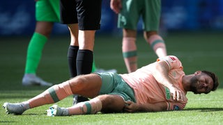Werder-Stürmer Niclas Füllkrug wälzt sich mit schmerzverzerrtem Gesicht am Boden.