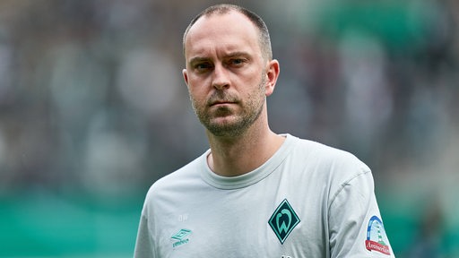 Werder_Trainer Ole Werner schreitet mit nachdenklichem Gesichtsausdruck über den Platz.