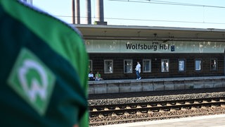 Die Werder-Raiute auf dem Trikot ist vor einem Schild mit der Aufschrift "Wolfsburg Hbf" zu sehen.
