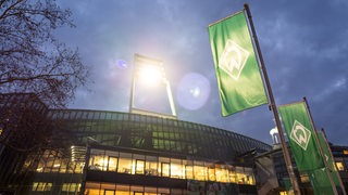 Das Weser-Stadion bei Nacht und von außen mit eingeschaltetem Flutlicht und den Werder-Fahnen im Vordergrund