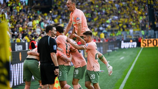 Traube von Werder-Spielern, die mit Oliver Burke dessen Siegtreffer in Dortmund feiern und auf ihn springen.