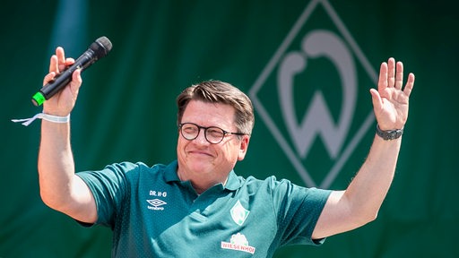 Werder-Präsident Hubertus Hess-Grunewald hebt lächelnd die Arme in die Höhe.