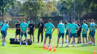 Werder-Coach Ole Werner hat beim Training seine Spieler um sich geschart und erklärt etwas.