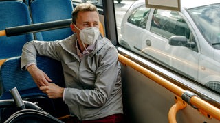 Ein Mann sitzt mit Maske in einem Bus.