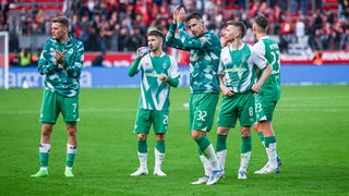 Werder-Spieler um Kapitän Marco Friedl stehen etwas ratlos auf dem Rasen, während er den Fans zuklatscht in Leverkusen.