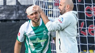 Werder-Stürmer Niclas Füllkrug bekommt von einem Betreuer einen Kopfverband angelegt.