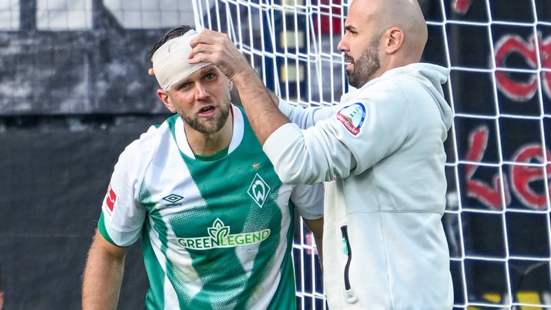 Werder-Stürmer Niclas Füllkrug bekommt von einem Betreuer einen Kopfverband angelegt.