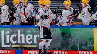 Eishockey-Spieler der Fischtown Pinguins stehen an der Bande und klatschen Nicholas Jensen ab.