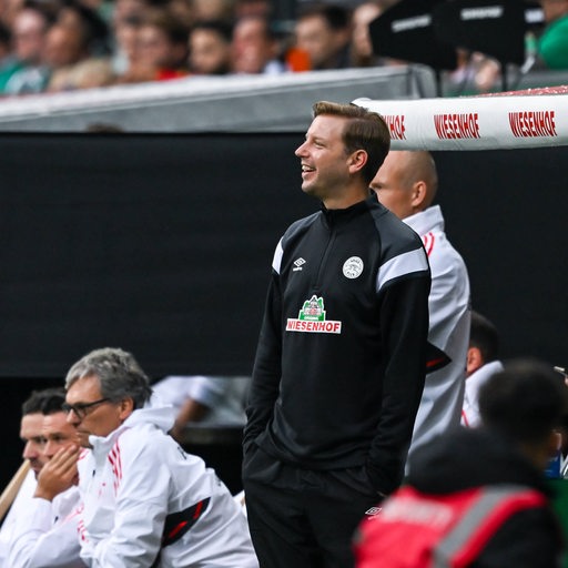 Ex-Werder-Trainer Florian Kohfeldt steht lächelnd an der Seitenlinie des Weser-Stadions beim Abschiedsspiel von Claudio Pizarro.