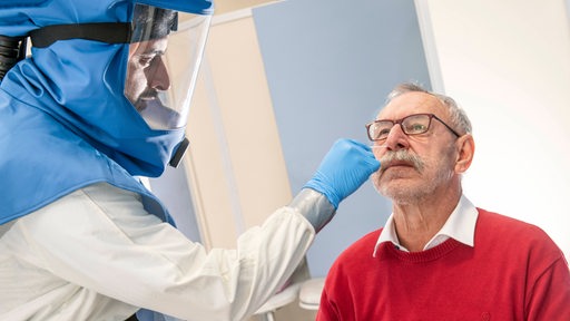 Ein Arzt mit Vollschutz macht einen Nasenabstrich bei einem Patienten