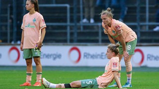 Fußball-Spielerinnen von Werder Bremen sitzen und stehen nach der Niederlage gegen Köln enttäuscht auf dem Rasen.