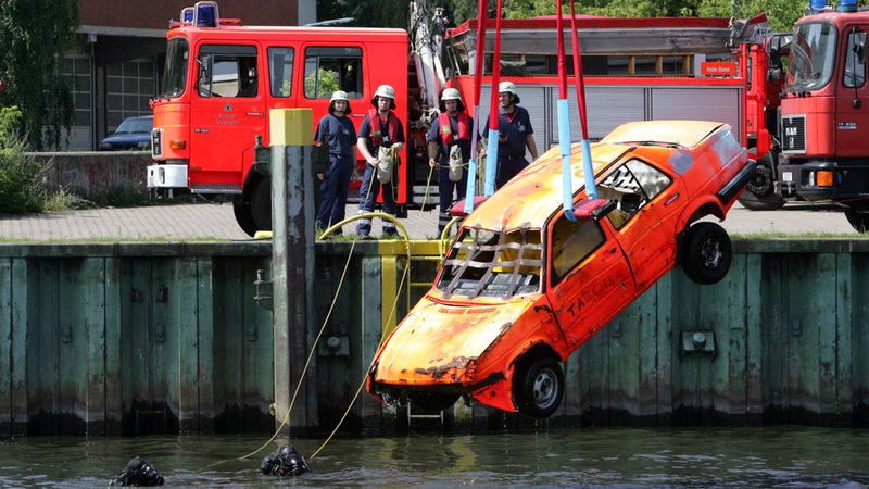 Feuerwehrleute retten ein Autowrack aus einem Hafenbecken.