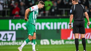 Werder-Stürmer Niclas Füllkrug hält sich im Spiel gegen Schalke mit schmerzverzerrtem Gesicht den Rücken.
