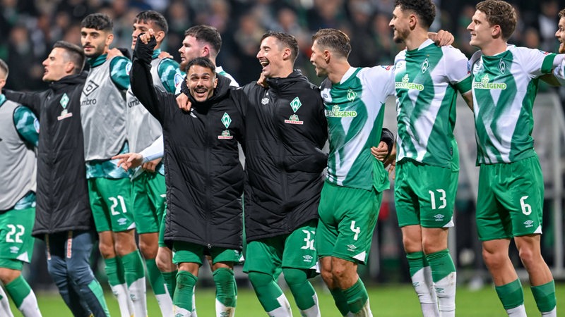 Werder-Spieler um Bittencourt und Friedl stehen Arm in Arm nach dem Spiel vor der Fankurve und feiern ausgelassen den Sieg.