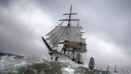 Das Segelschulschiff Gorch Fock fährt unter wolkigem Himmel durch aufgewühltes Wasser