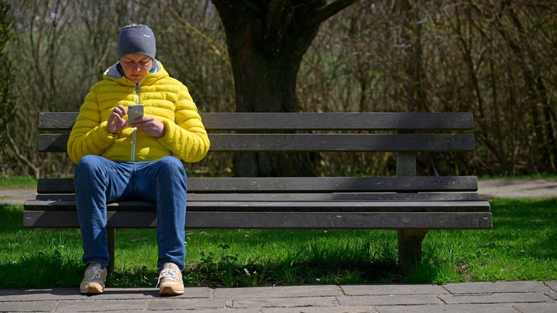 Mann sitzt auf Parkbank und guckt aufs Handy
