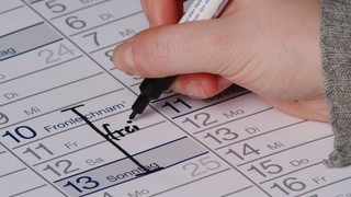 Eine Hand schreibt mit einem Filzstift das Wort "Frei" in einem Kalender.