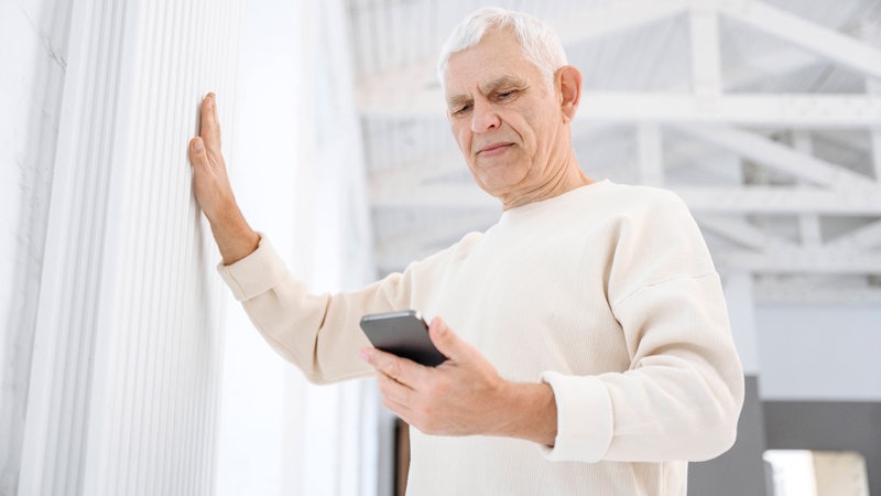 Ein älterer Mann schaut auf sein Handy.