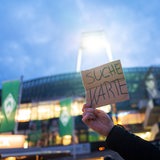 Vor dem Weser-Stadion hält ein Fans ein Pappschild hoch mit der Aufschrift "Suche Karte".