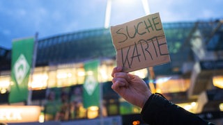 Vor dem Weser-Stadion hält ein Fans ein Pappschild hoch mit der Aufschrift "Suche Karte".